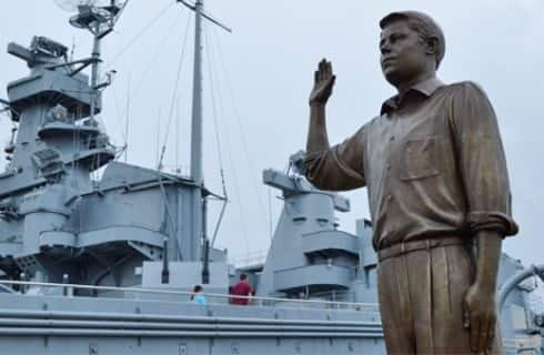 Bronze statue of a man next to large naval ship