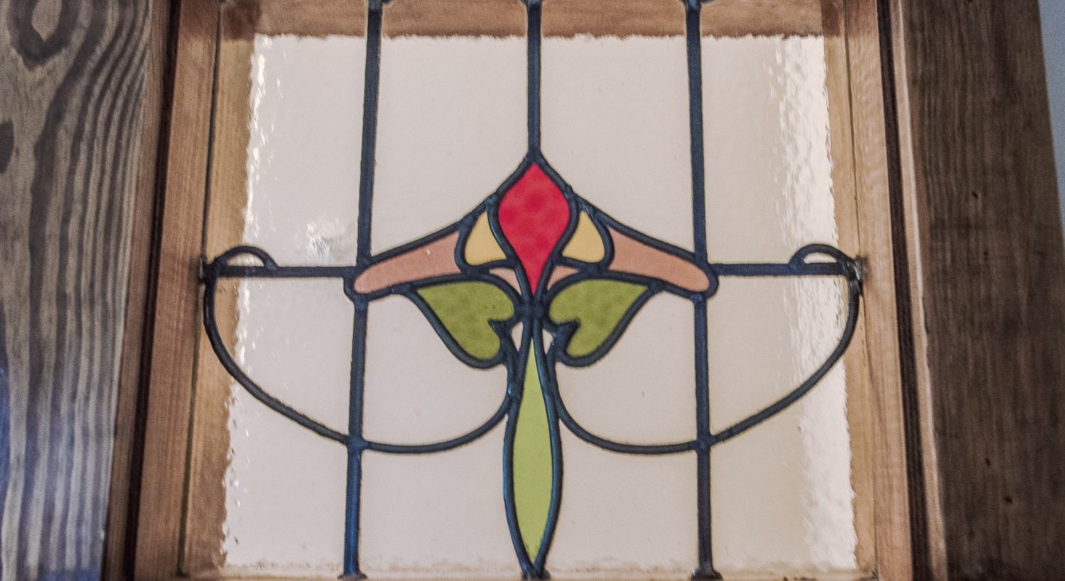 Wooden door with stained glass insert of a red, yellow, and pink flower with green stem