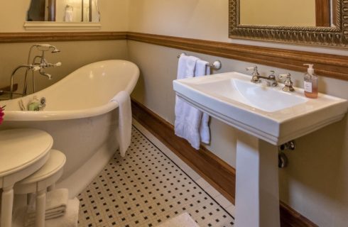 Bathroom with light tan walls, wooden chair rail and trim, black and white tiled floor, large white bathtub, and white vanity