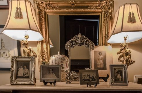 Victorian dresser with antique pictures and frames on top and two lamps with antique mirror hanging above